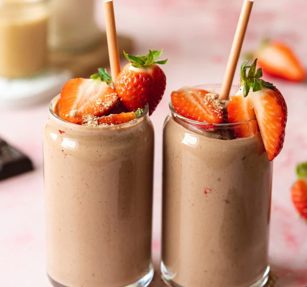 Two strawberry smoothies in glasses topped with fresh strawberries